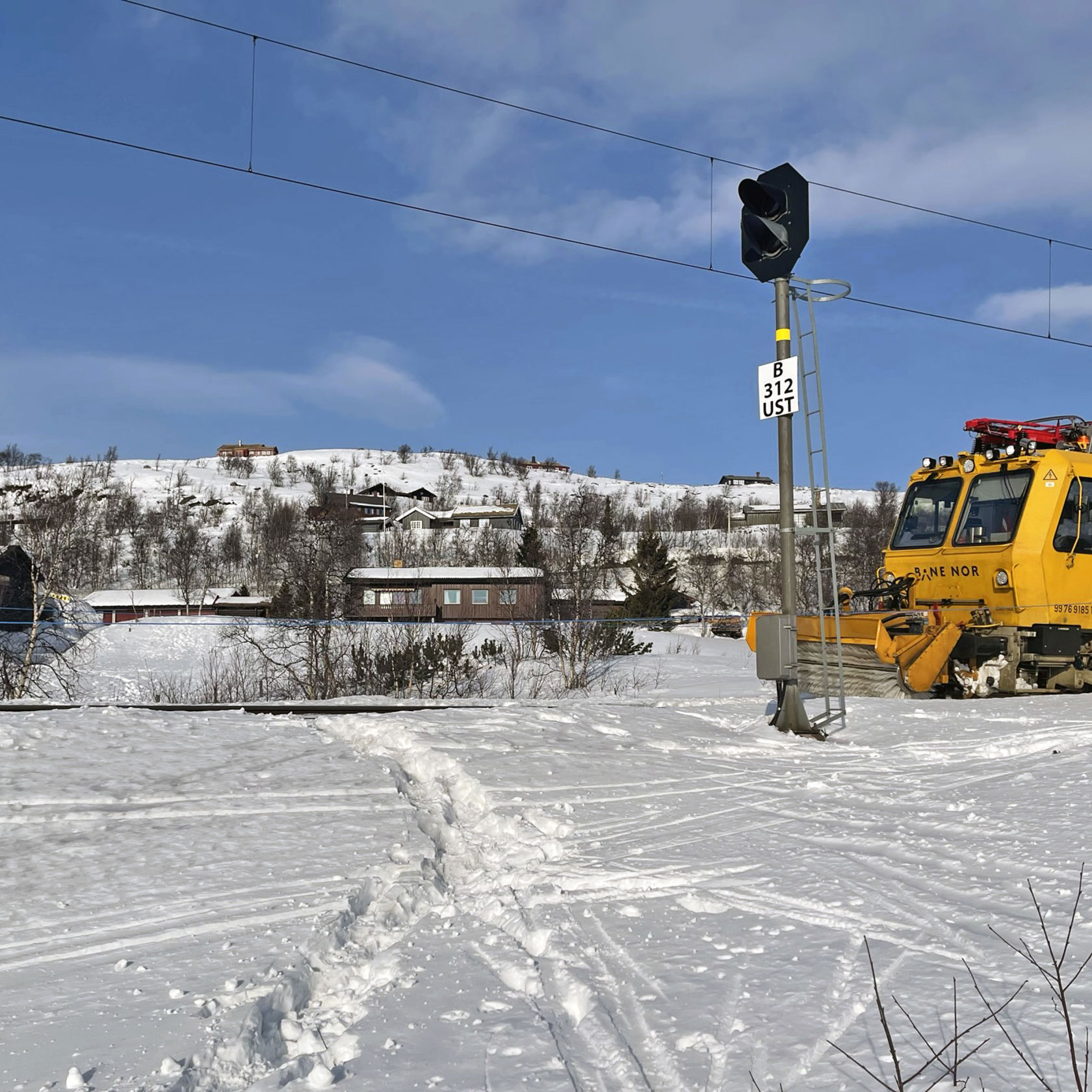 Spor i snøen krysser jernbaneskinnene. En gul arbeidsmaskin fra Bane NOR står på sporet.