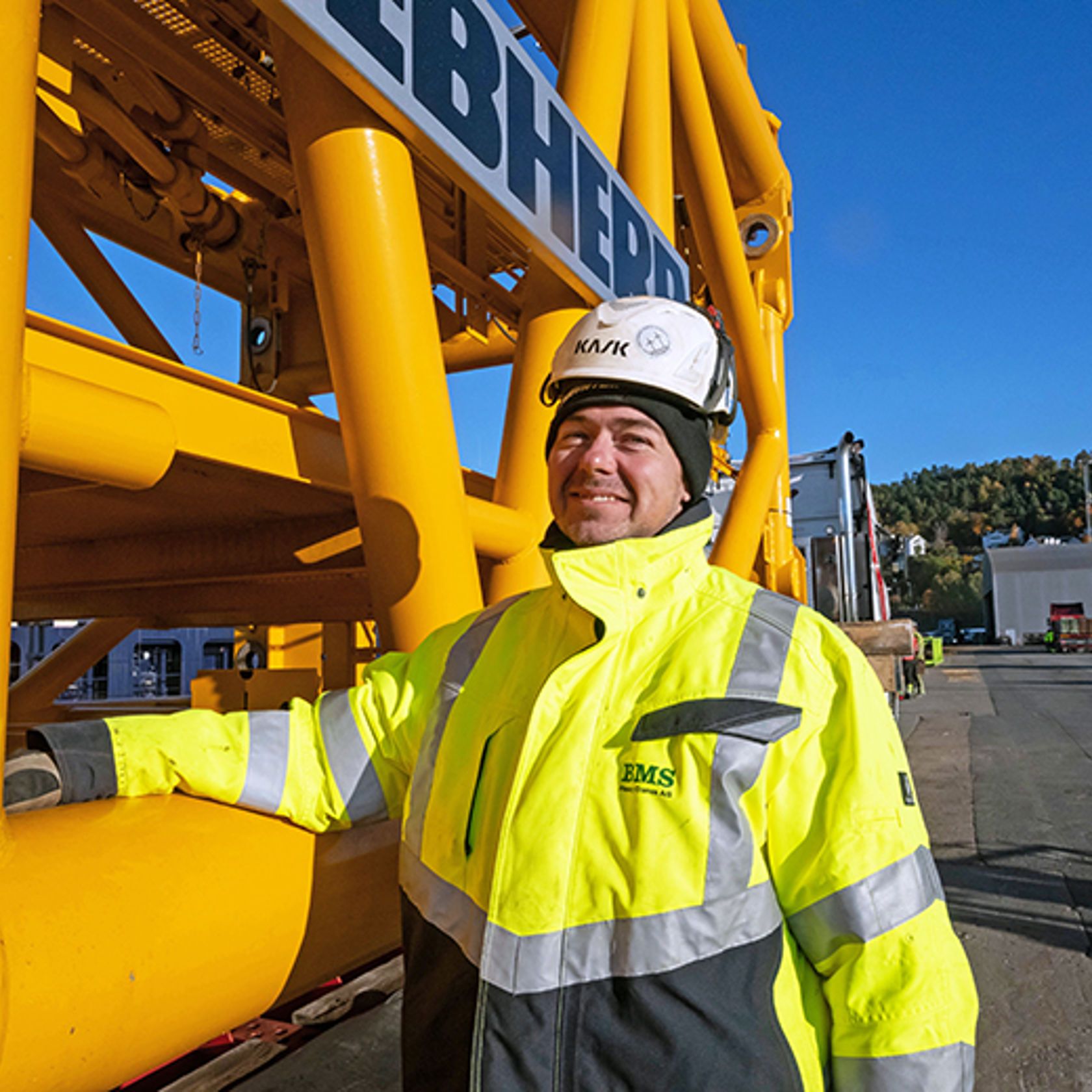 Mann i hjelm og gule arbeidsklær stående ved en gul maskin.