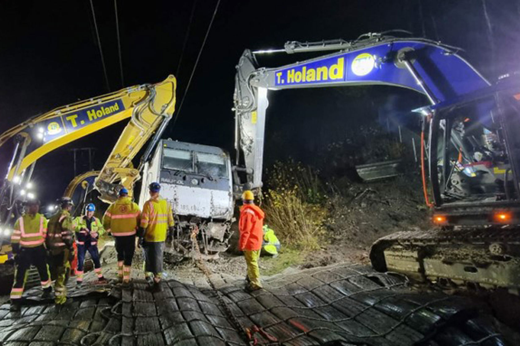 Bilde av en arbeidsgjeng og to gravemaskiner ved et avsporet tog.