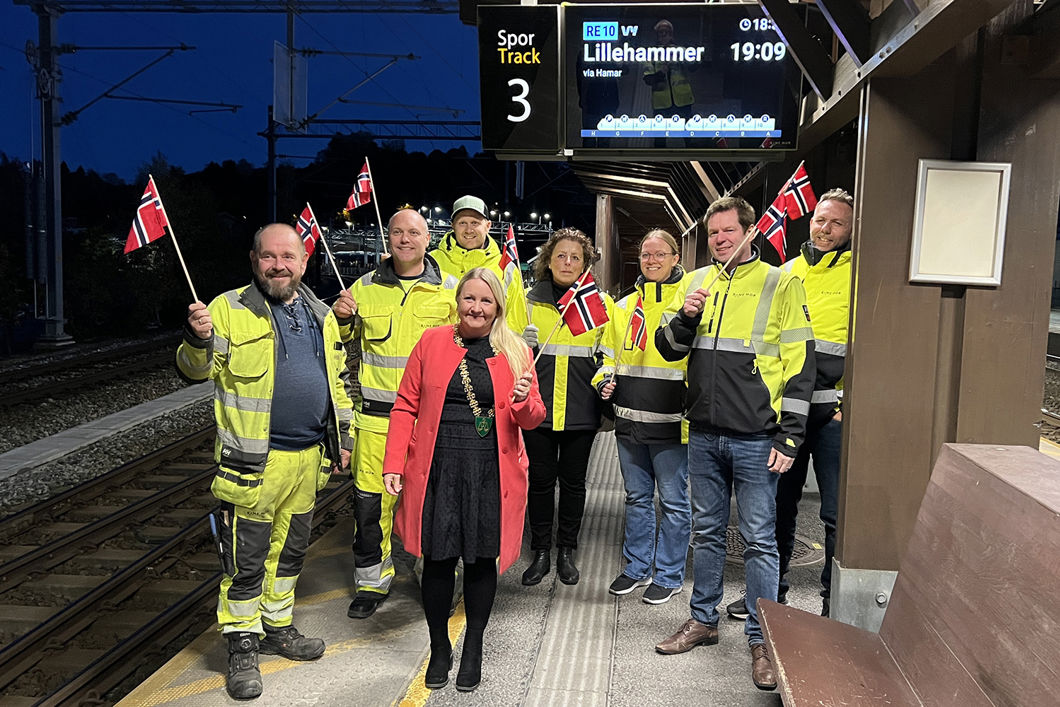 Blide folk vifter med flagg på plattformen ved Eidsvoll stasjon.