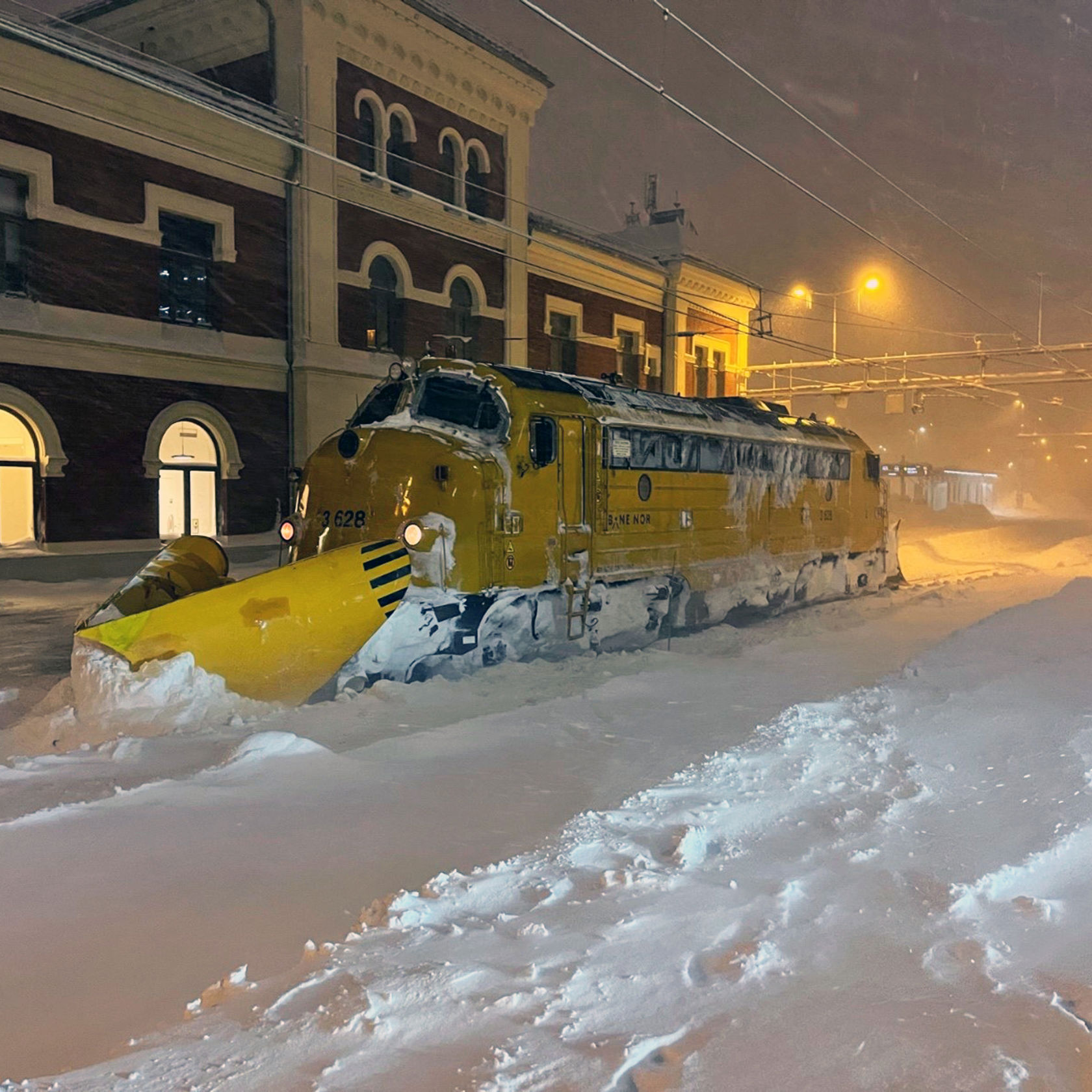 Arbeidstog med snøskuffe foran står parkert inne på en stasjon.