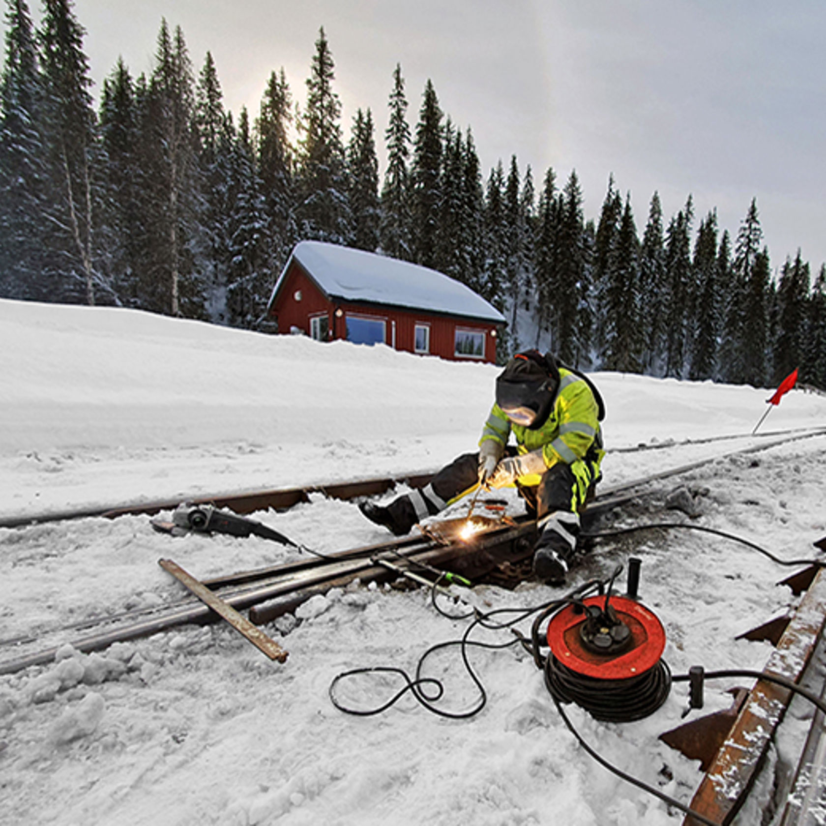 En person sitter på baken midt i et spor og sveiser skinnegangen.