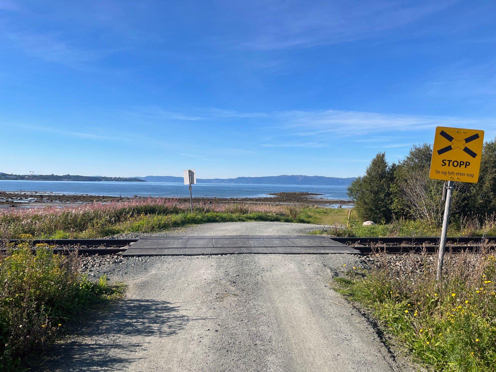 Enkel planovergang i kystlandskap med havet i bakgrunn.