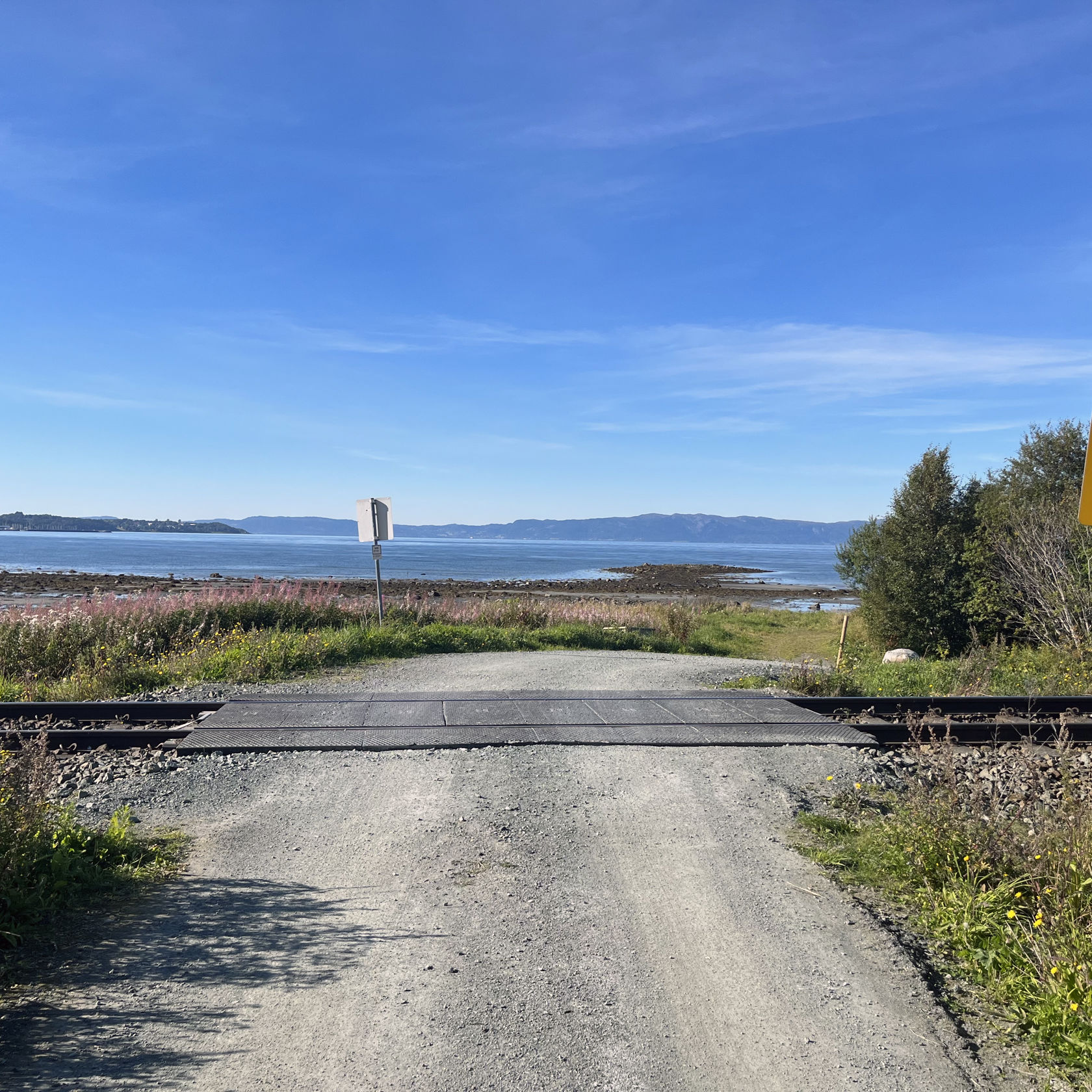 Enkel planovergang i kystlandskap med havet i bakgrunn.