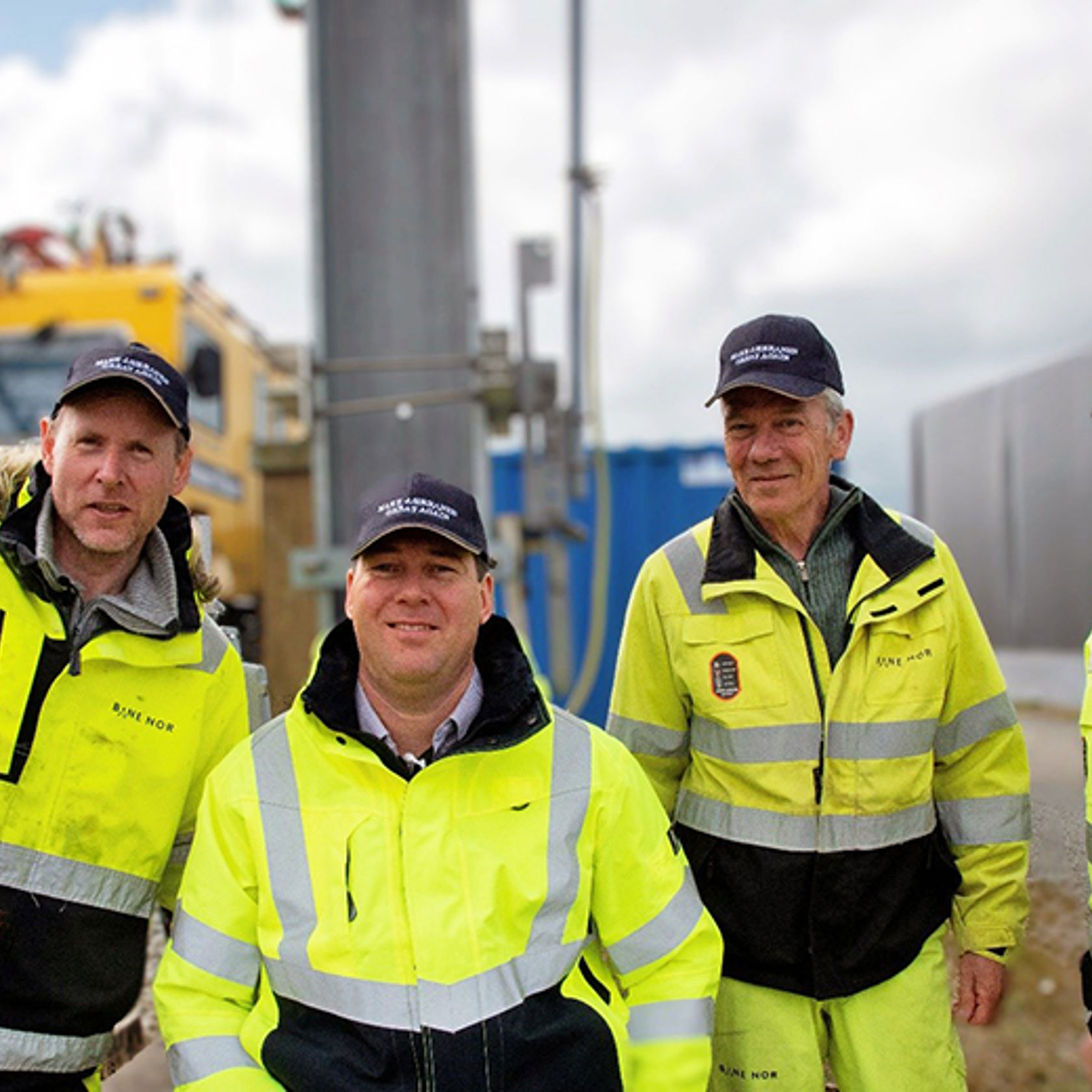 Ansatte på jernbanen i vernetøy og med caps på hodet, foran en stor gul maskin.