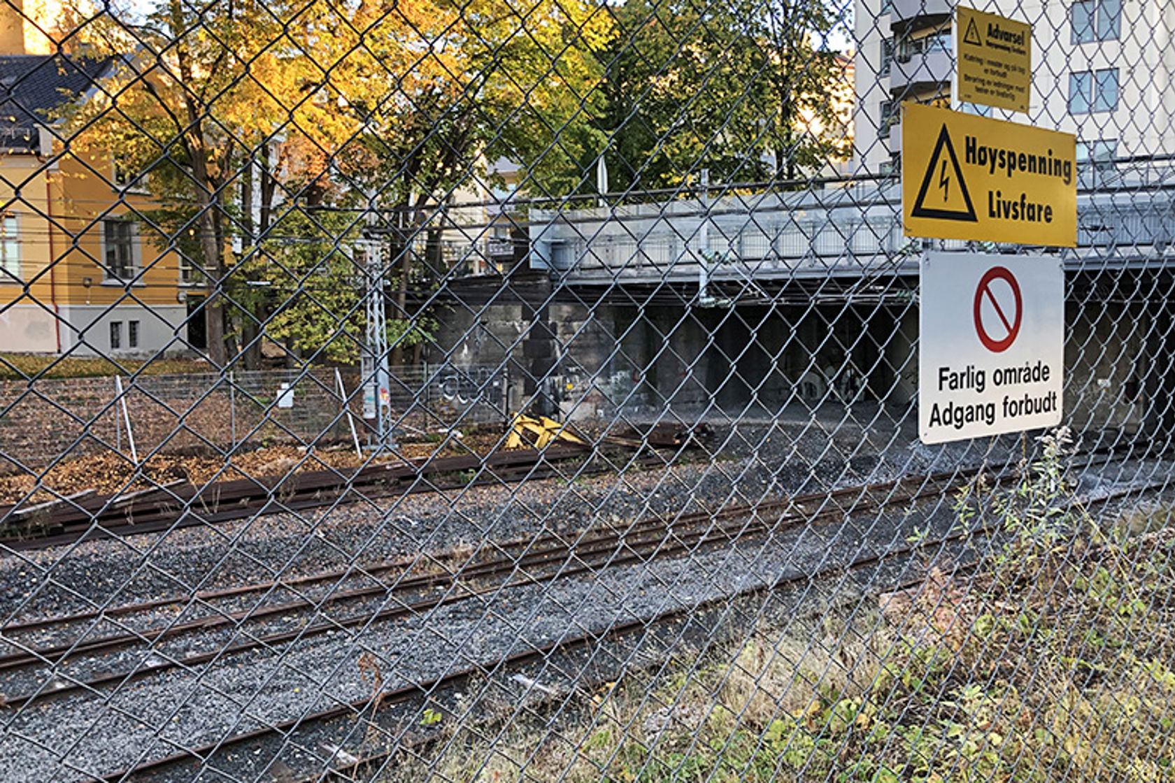 Bildet viser et gjerde, og bak gjerde er det et jernbaneområde med spor og tunnelportal