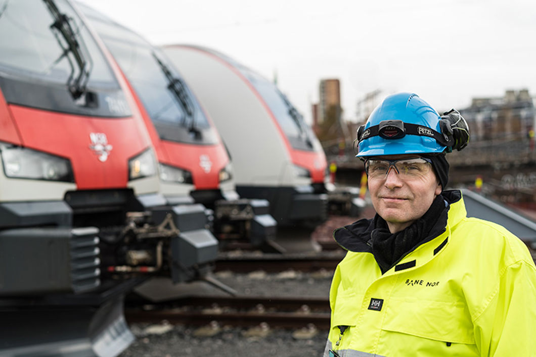 Mann i vernetøy står foran to parkerte tog. 