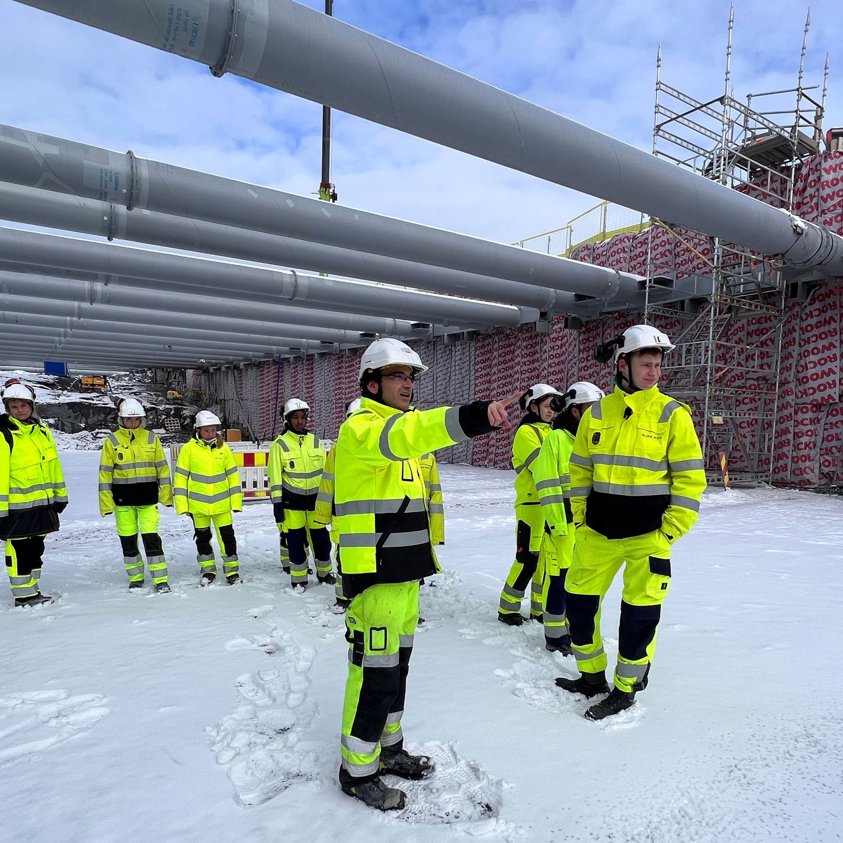 Menn og kvinner i verneutstyr står i snødekt kulvert. I bakgrunnen sees avstivere og spuntvegg.