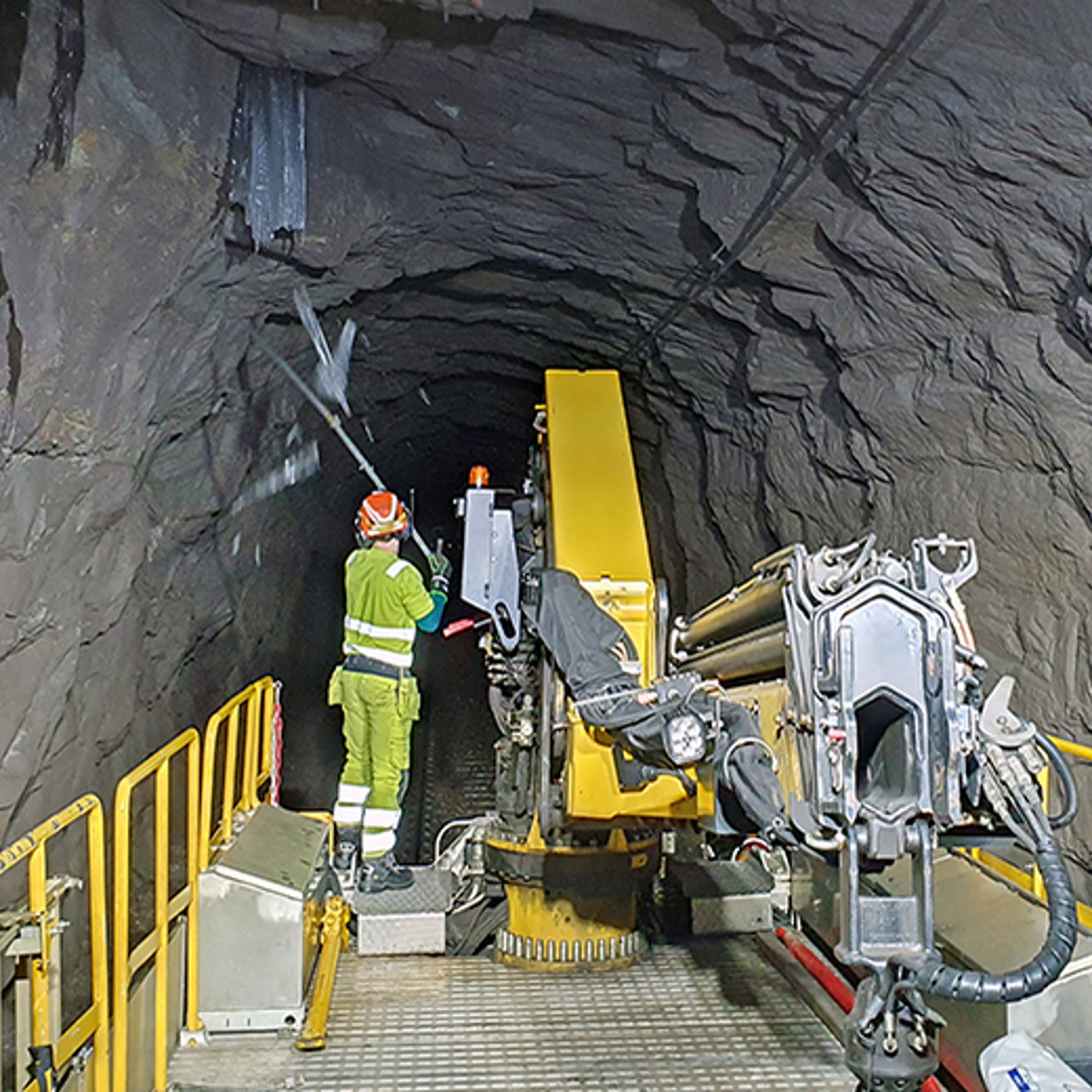 En mann står bakerst på et arbeidstog i tunnel og slår ned istapper fra tunneltaket.