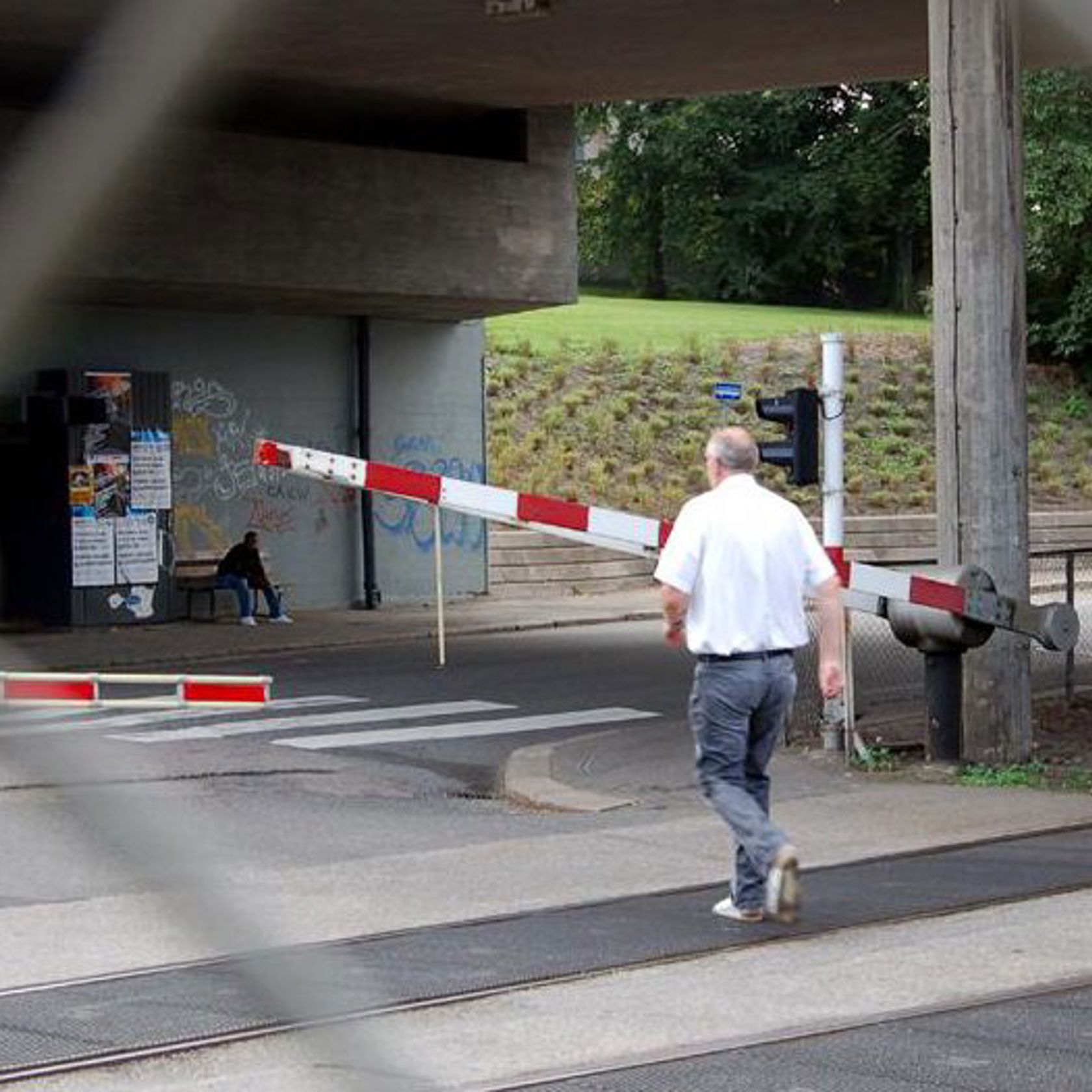 En mann er på vei gående mot en planovergang der bommene går ned.