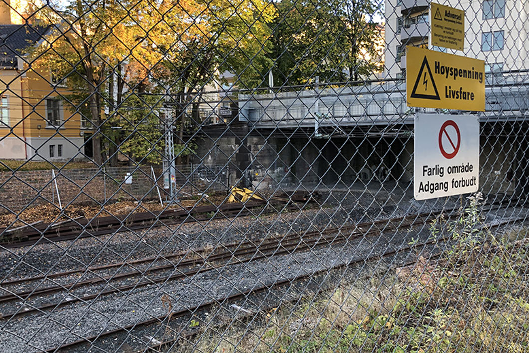 Bildet viser et gjerde som gjerder inn et jernbaneområde med skinner og tunnel. 