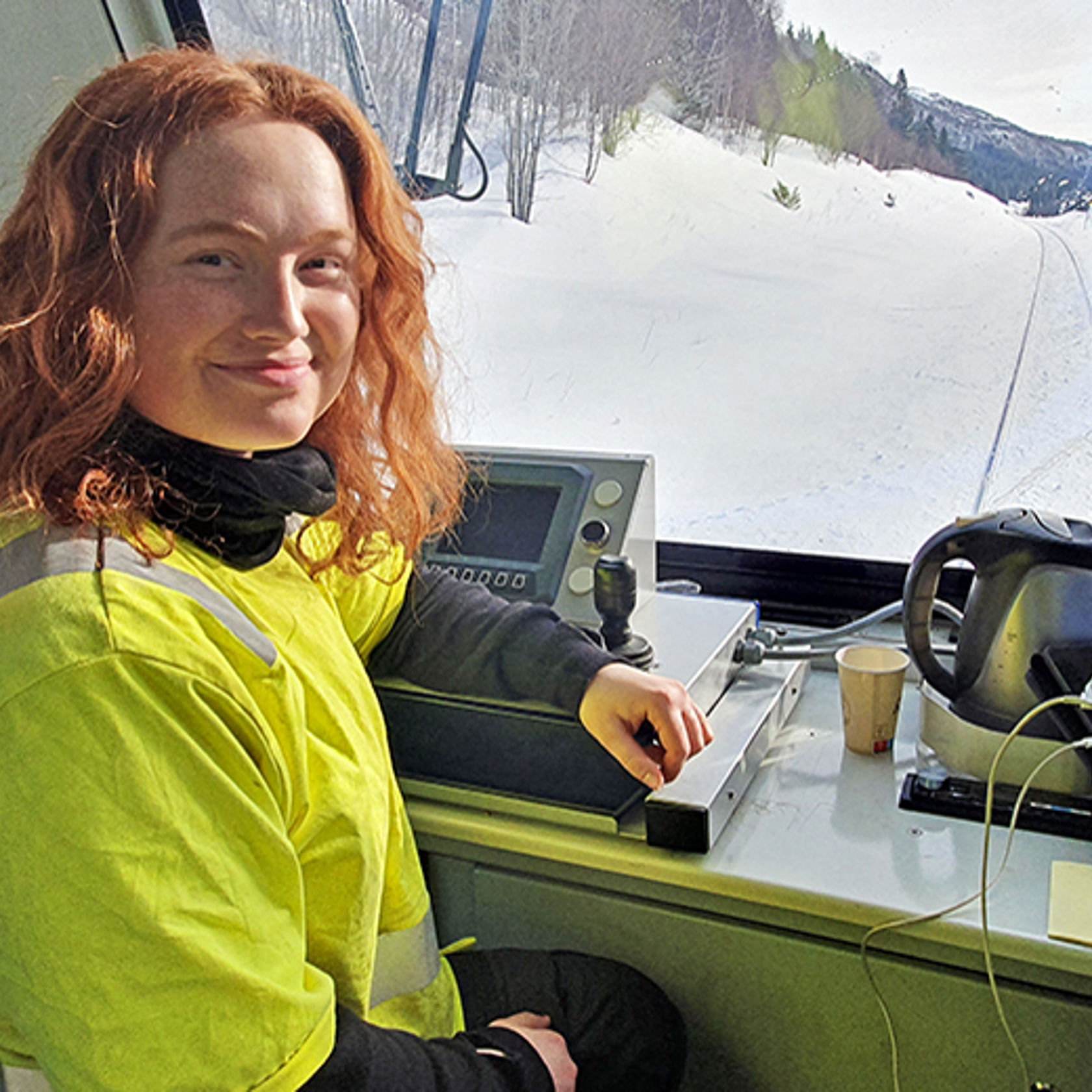 En ung kvinne i arbeidstøy sitter ved spakene i et arbeidstog på jernbanen.