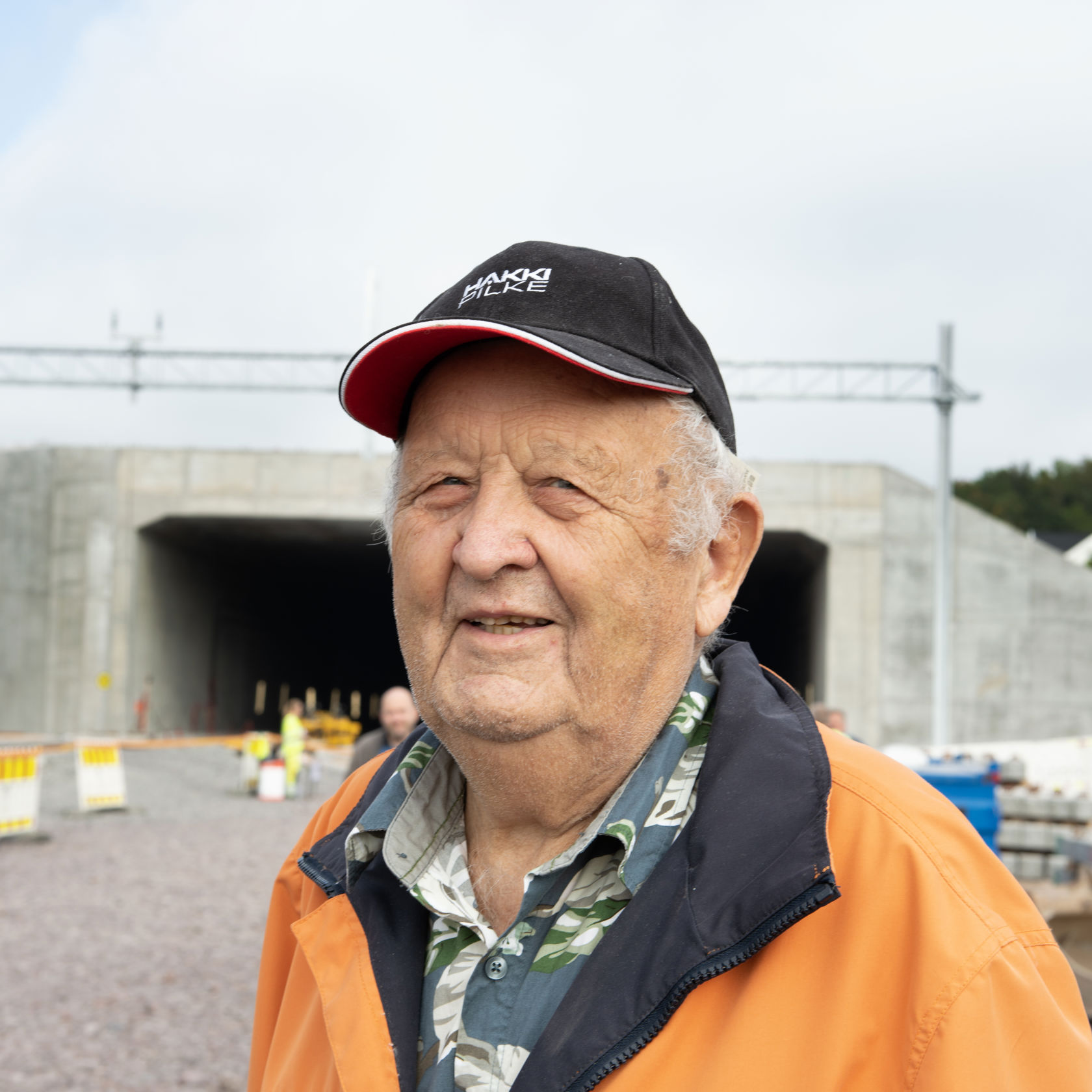 Eldre mann med oransje jakke og svart cap