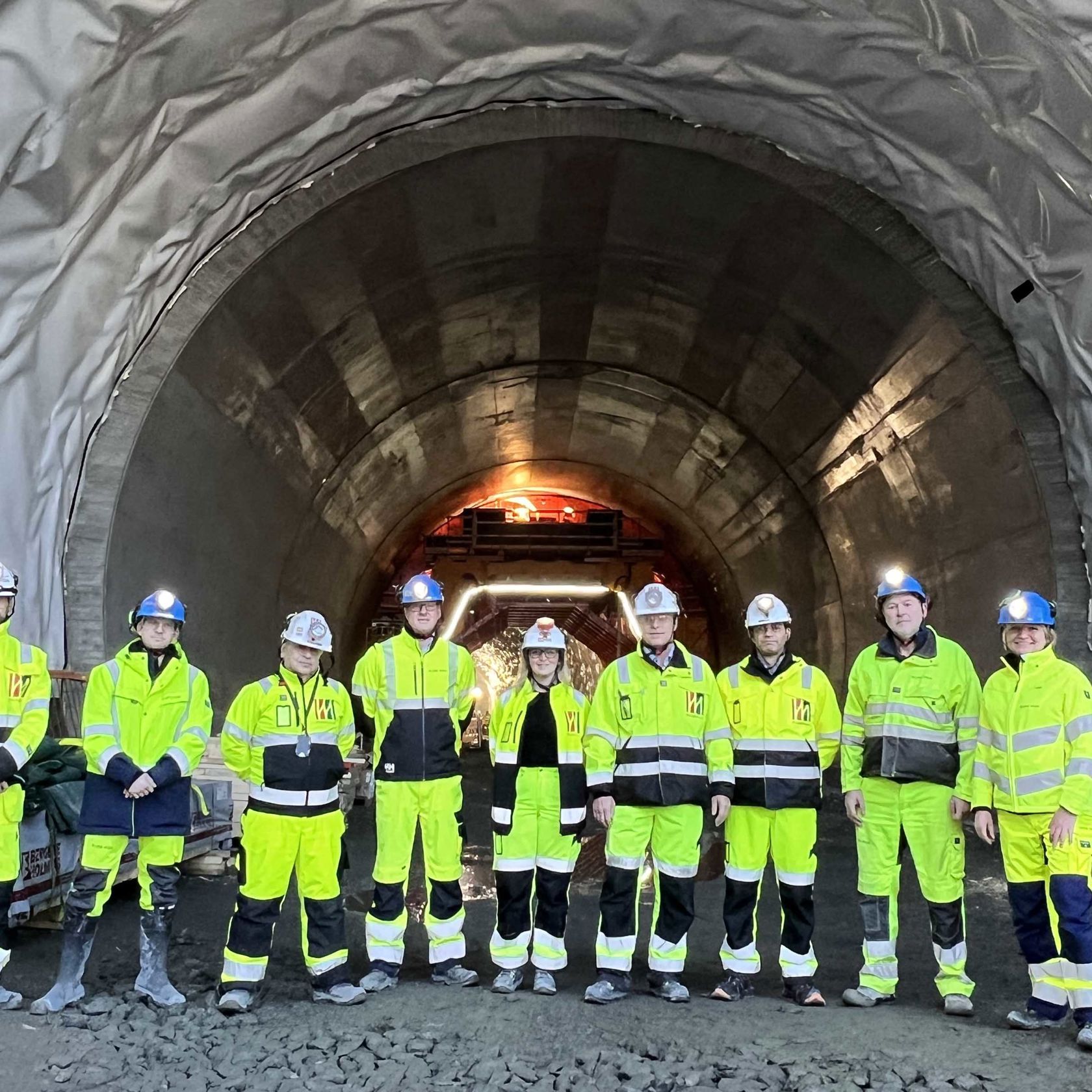 Kvinner og menn i vernetøy står oppstilt utenfor tunnel.