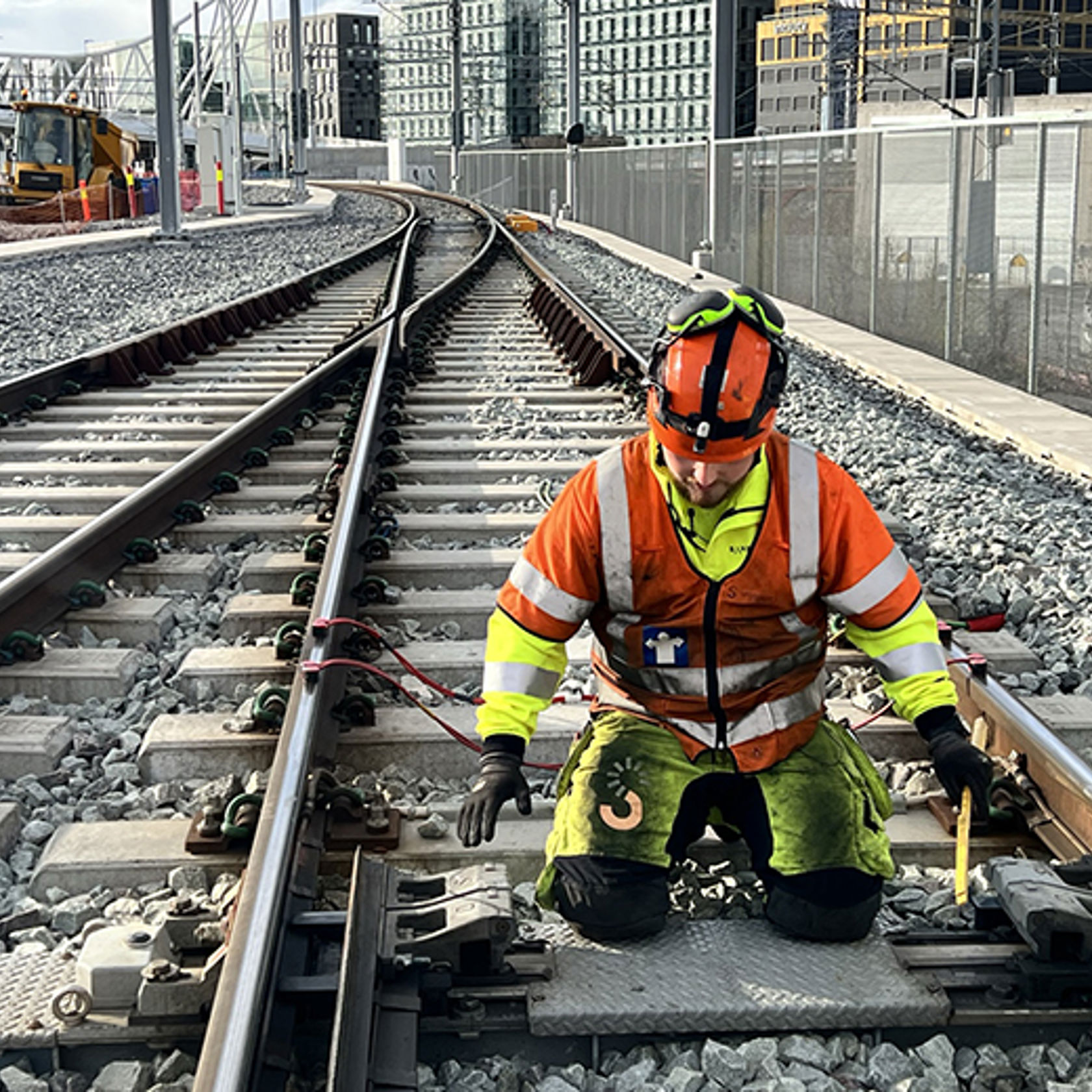 Mann i gult og oransje arbeidstøy jobber i jernbanespor.